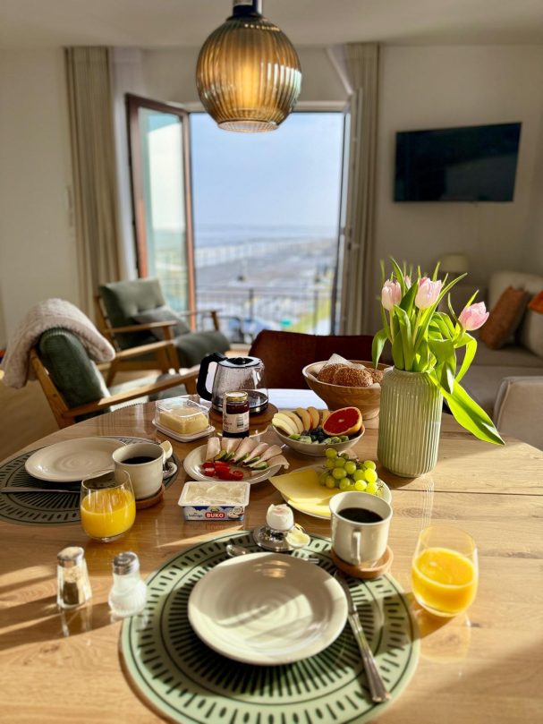Frühstück in der Ferienwohnung Meerzeit Pellworm Frühstückstisch in der Ferienwohnung auf Pellworm mit Blick ins helle Wohnzimmer und der Nordsee im Hintergrund